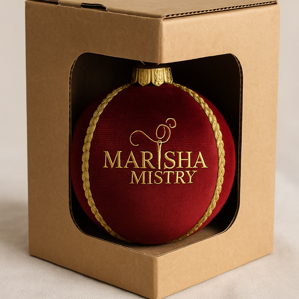 Red ornament with 'Marisha Mistry' branding in a cardboard box on a beige background