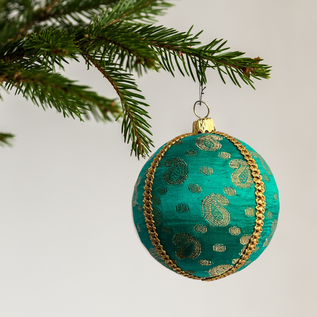 Decorative green ornament with gold patterns hanging on a Christmas tree branch.