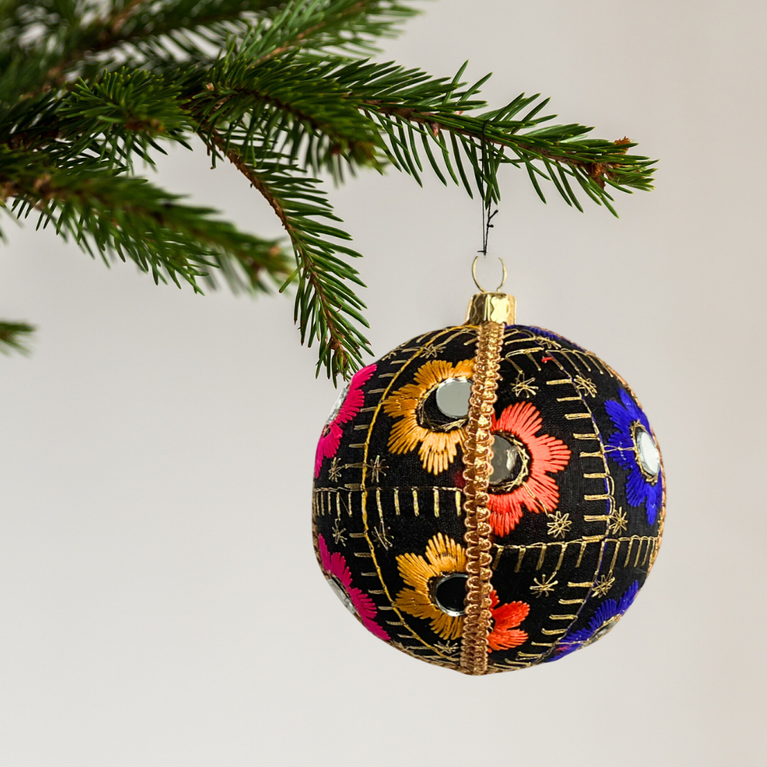 Decorative Christmas ball ornament with floral patterns hanging on a tree branch.