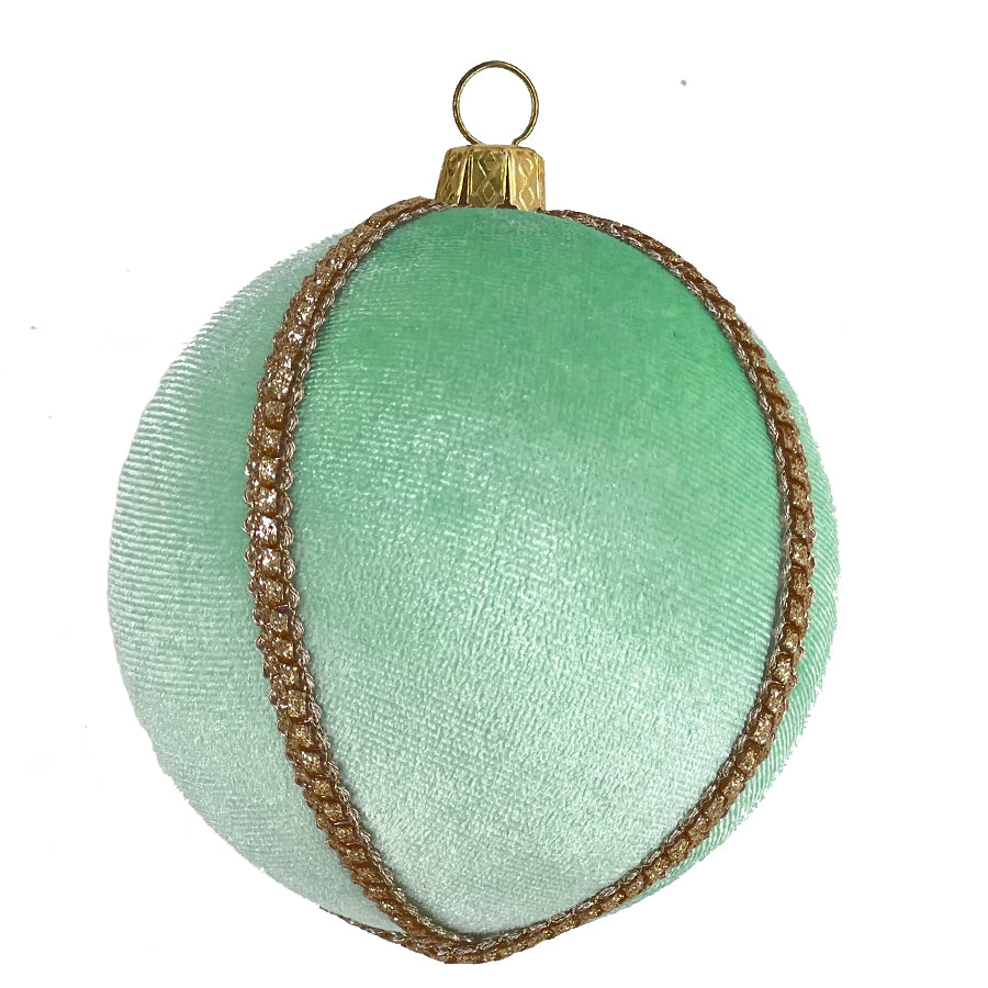Close-up of a single mint green velvet bauble with criss-cross gold trim and a gold hanging cap, on a white background.