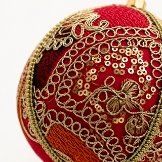 A cluster of Aarna handmade fabric baubles, 10cm, grouped to show the sweeping gold zari cord goldwork in paisley and floral forms with dense gold sequins.