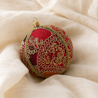 Aarna fabric bauble styled on linen, a 10cm handmade ornament with sweeping gold zari cord goldwork in paisley and floral forms with dense gold sequins.