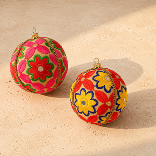 Advik bauble hanging with soft bokeh lights, showing its warm cream ground and large-scale hand-embroidered daisy and sunflower motifs with shisha mirror centres.