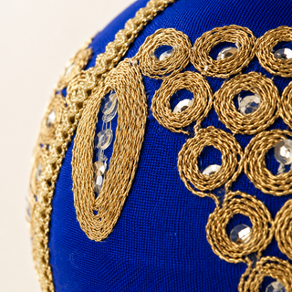 Arjun bauble detail shot, a 10cm UK-made sustainable ornament with royal blue ground and a cascading cluster of gold mirror-work medallions with an elongated leaf motif.
