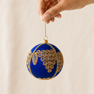Arjun bauble hanging with soft bokeh lights, showing its royal blue ground and a cascading cluster of gold mirror-work medallions with an elongated leaf motif.
