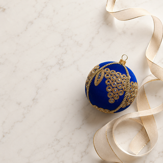 Arjun fabric bauble styled on linen, a 10cm handmade ornament with a cascading cluster of gold mirror-work medallions with an elongated leaf motif.