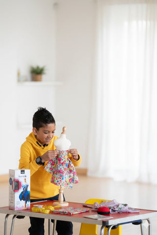 Child in yellow hoodie playing with a doll on a table in a bright room.