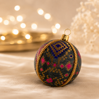 Chirag bauble hanging with soft bokeh lights, showing its charcoal ground and a dense gold checkerboard pattern lifted by magenta and cobalt blue accents.