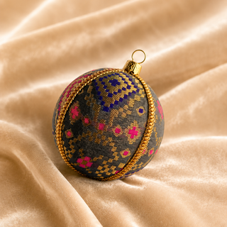 Chirag bauble detail shot, an 8cm UK-made sustainable ornament with charcoal ground and a dense gold checkerboard pattern lifted by magenta and cobalt blue accents.