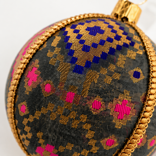 Chirag fabric bauble styled on linen, an 8cm handmade ornament with a dense gold checkerboard pattern lifted by magenta and cobalt blue accents.