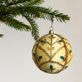 Decorative gold Lalit Christmas ball ornament with green accents hanging on a tree branch.