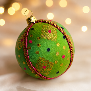 Jaya bauble detail shot, an 8cm UK-made sustainable ornament with vivid green ground and gold diamond-lattice motifs with playful pink and navy dots.