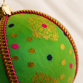 Jaya fabric bauble styled on linen, an 8cm handmade ornament with gold diamond-lattice motifs with playful pink and navy dots.