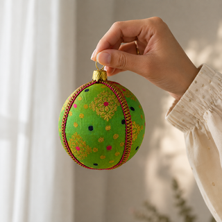 Jaya bauble hanging with soft bokeh lights, showing its vivid green ground and gold diamond-lattice motifs with playful pink and navy dots.