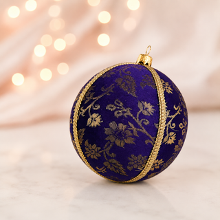 Close-up of the Kaasni bauble showing sweeping gold floral scrollwork brocade with a fine cord seam trim on deep purple reclaimed fabric.