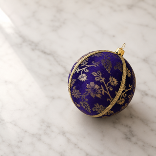 Kaasni fabric bauble styled on linen, an 8cm handmade ornament with sweeping gold floral scrollwork brocade with a fine cord seam trim.