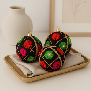 Decorative Kalyani Christmas ornaments with colourful patterns on a wooden tray. Kalyani Bauble – sustainable fabric decoration with pink, green & red embroidery on a black base, handmade in Britain.
