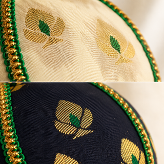 Kamla bauble detail shot, an 8cm UK-made sustainable ornament with soft cream (also in black) ground and a delicate gold floral motif with green accents and a green-and-gold cord trim.