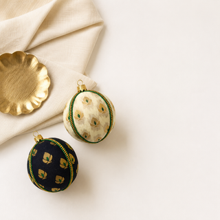 Kamla fabric bauble styled on linen, an 8cm handmade ornament with a delicate gold floral motif with green accents and a green-and-gold cord trim.
