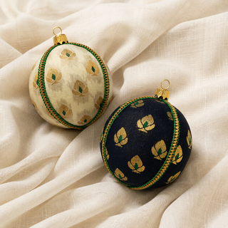 Kamla handmade fabric bauble on a marble surface, 8cm, showing a delicate gold floral motif with green accents and a green-and-gold cord trim on a soft cream (also in black) ground.