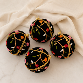Four round black velvet Christmas ornaments with gold braided trim and embroidered floral patterns, arranged on a cream fabric surface.