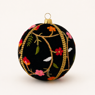A round black Christmas ornament decorated with colorful floral embroidery in pink, red, orange, and green, accented by gold braided trim and a gold hanging loop at the top, shown against a plain off-white background.