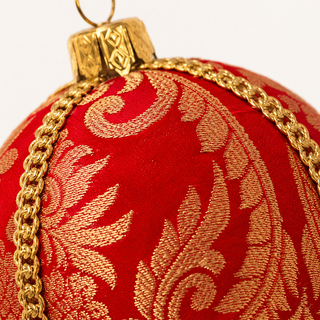 A close-up of a red Christmas ornament with a gold damask pattern and a gold chain detail, featuring a gold cap and loop at the top.