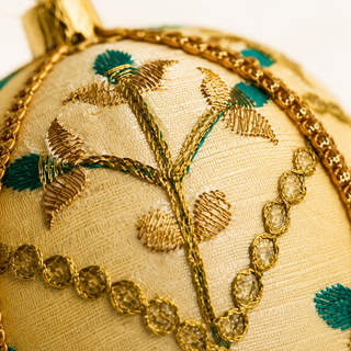 Lalit bauble detail shot, a 10cm UK-made sustainable ornament with ivory and gold ground and delicate gold floral embroidery with teal thread accents and a metallic gold trim.