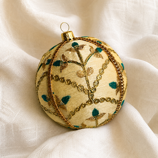 Lalit bauble hanging with soft bokeh lights, showing its ivory and gold ground and delicate gold floral embroidery with teal thread accents and a metallic gold trim.