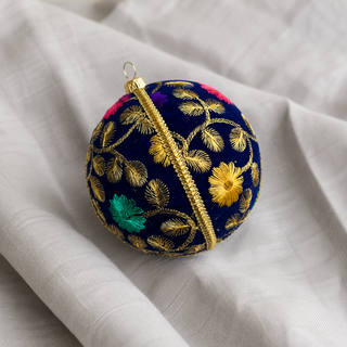 Mahir fabric bauble styled on linen, a 10cm handmade ornament with fine gold fern-leaf embroidery with scattered pink, purple and teal florals.