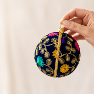 Mahir bauble detail shot, a 10cm UK-made sustainable ornament with deep navy ground and fine gold fern-leaf embroidery with scattered pink, purple and teal florals.