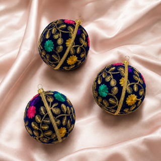 Mahir handmade fabric bauble on a marble surface, 10cm, showing fine gold fern-leaf embroidery with scattered pink, purple and teal florals on a deep navy ground.