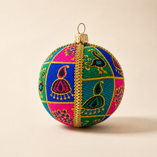 A spherical embroidered Christmas ornament with a gold hanging loop, featuring a vibrant multicolor design of pink, blue, and green panels with peacock motifs and a central gold braided stripe, set against a solid beige background.
