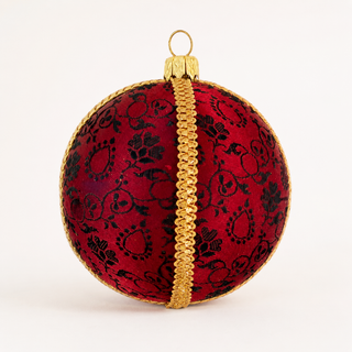 A round red Christmas ornament with a black floral damask pattern, a central gold braided stripe, and a gold hanging loop at the top, shown on a plain white background.