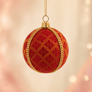 A red and gold patterned Christmas ornament hanging from a gold string against a soft, warm bokeh background.