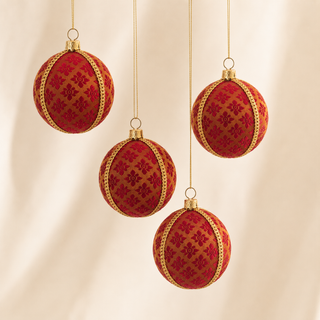 Four hanging red Christmas ornaments with gold trim and a floral pattern, suspended against a soft cream fabric backdrop.