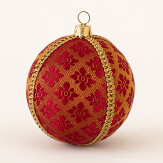 A spherical Christmas ornament featuring a red floral pattern on a gold background, accented with a gold braided trim and a gold hanging loop at the top.
