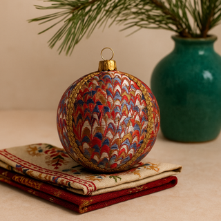 Decorative Christmas ball ornament with intricate patterns on a textured surface with a vase and branches in the background.
