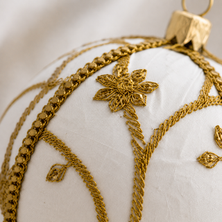Shashi bauble detail shot, a 10cm UK-made sustainable ornament with ivory ground and raised gold zardozi embroidery in a sweeping vine and trellis pattern with beaded flowers.