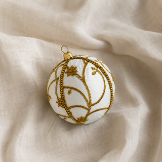Shashi fabric bauble styled on linen, a 10cm handmade ornament with raised gold zardozi embroidery in a sweeping vine and trellis pattern with beaded flowers.