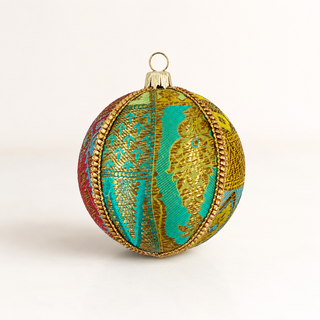 A spherical Christmas ornament decorated with a vibrant, multicolored pattern featuring turquoise, gold, pink, and green, accented by a gold beaded border and a gold hanging loop at the top.