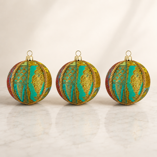 Three round decorative Christmas ornaments with a gold and turquoise map pattern, displayed on a light marble surface against a soft white background.