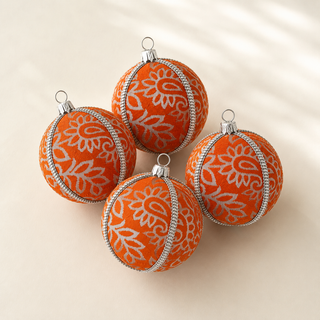 Four orange fabric Christmas ornaments with white floral patterns and silver trim, arranged on a light beige background.