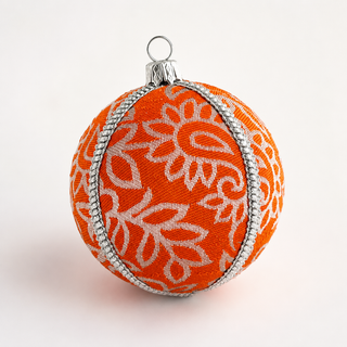 An orange Christmas ornament with a white floral pattern and silver trim, featuring a silver hanging loop at the top, set against a plain white background.