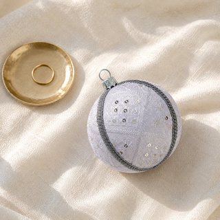Snow Queen fabric bauble styled on linen, a 10cm handmade ornament with a diamond-quilted stitch pattern with delicate starburst embroidery, scattered sequins and a silver cord trim.