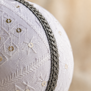 Snow Queen bauble hanging with soft bokeh lights, showing its white ground and a diamond-quilted stitch pattern with delicate starburst embroidery, scattered sequins and a silver cord trim.