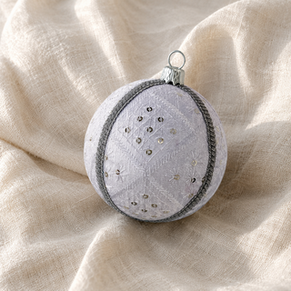 Close-up of the Snow Queen bauble showing a diamond-quilted stitch pattern with delicate starburst embroidery, scattered sequins and a silver cord trim on white reclaimed fabric.