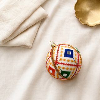 Sohan bauble detail shot, a 10cm UK-made sustainable ornament with crisp white ground and bold red diagonal lines with a fine gold star-stitch pattern and mirror-centred diamonds.