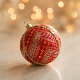 Subhash bauble detail shot, an 8cm UK-made sustainable ornament with deep red silk ground and diagonal bands of gold and silver embroidery with scattered sequin florets and a beaded gold trim.