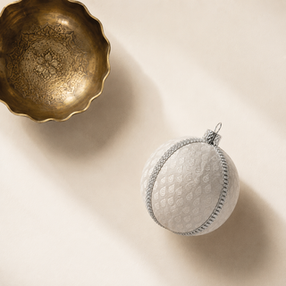 Surya bauble hanging with soft bokeh lights, showing its soft ivory ground and a woven brocade leaf motif with a fine silver diamanté trim.